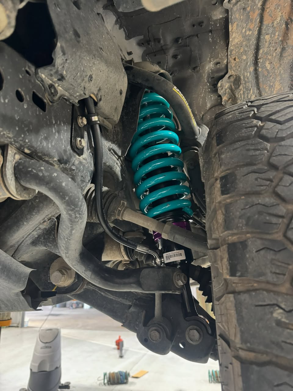 A teal coil over suspension unit fitted to a four wheel drive, seen from underneath on the hoist